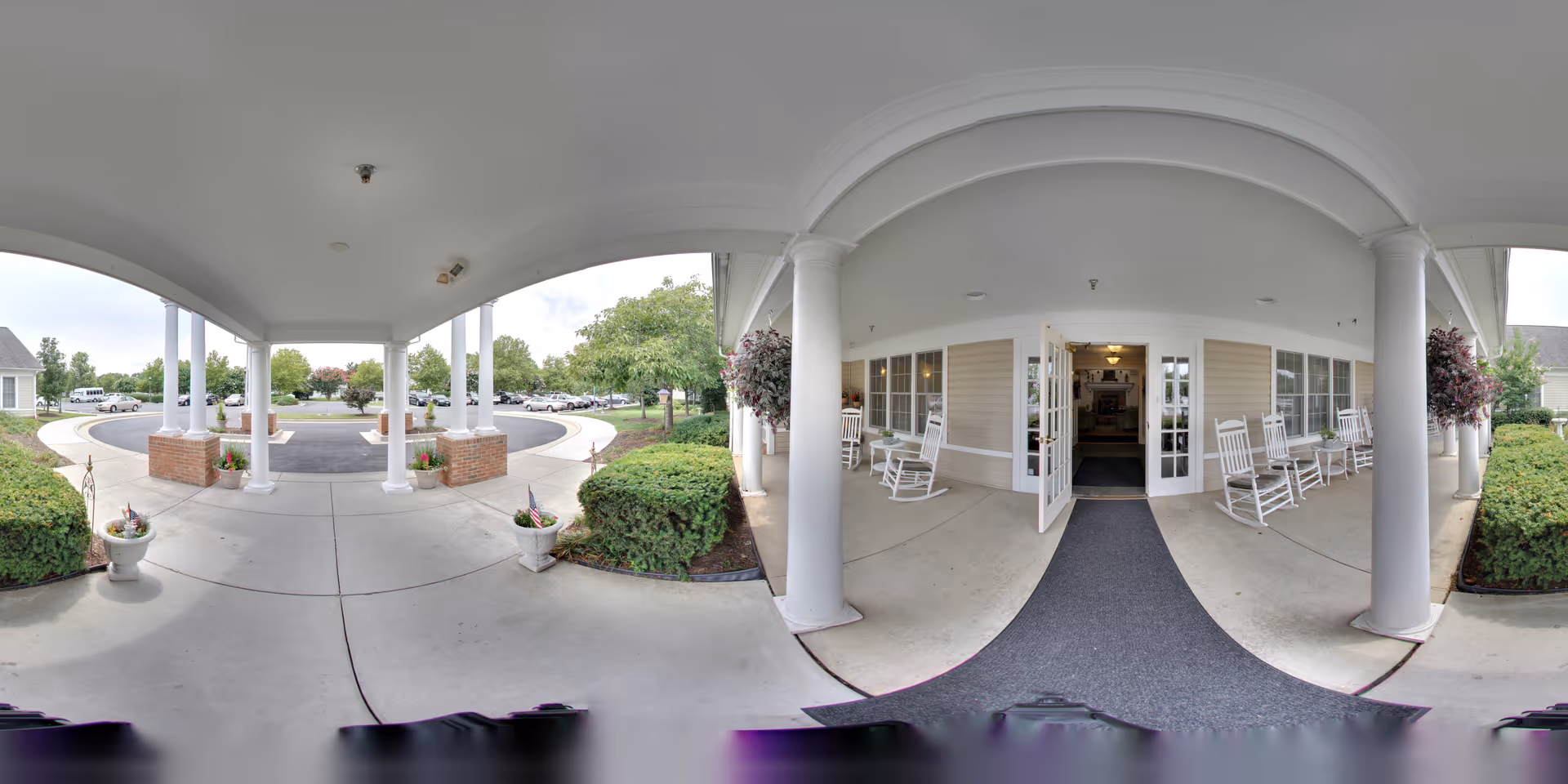 Covered front entrance with white columns, rocking chairs, shrubs, and a circular drive at an assisted living facility.