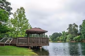 A wooden gazebo on a deck overlooking a calm lake surrounded by trees under a cloudy sky.