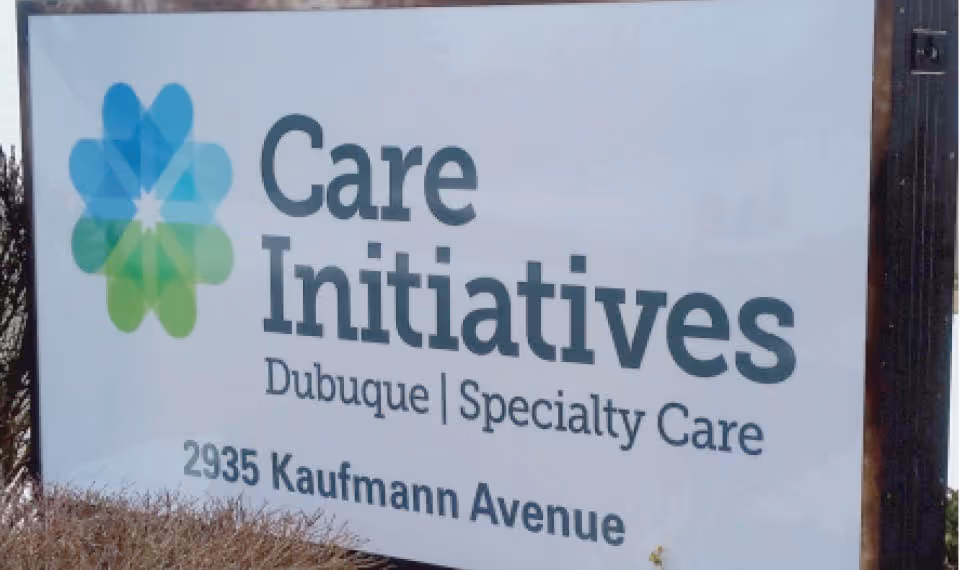 Outdoor sign reading "Care Initiatives Dubuque | Specialty Care 2935 Kaufmann Avenue" with a green-blue flower logo.