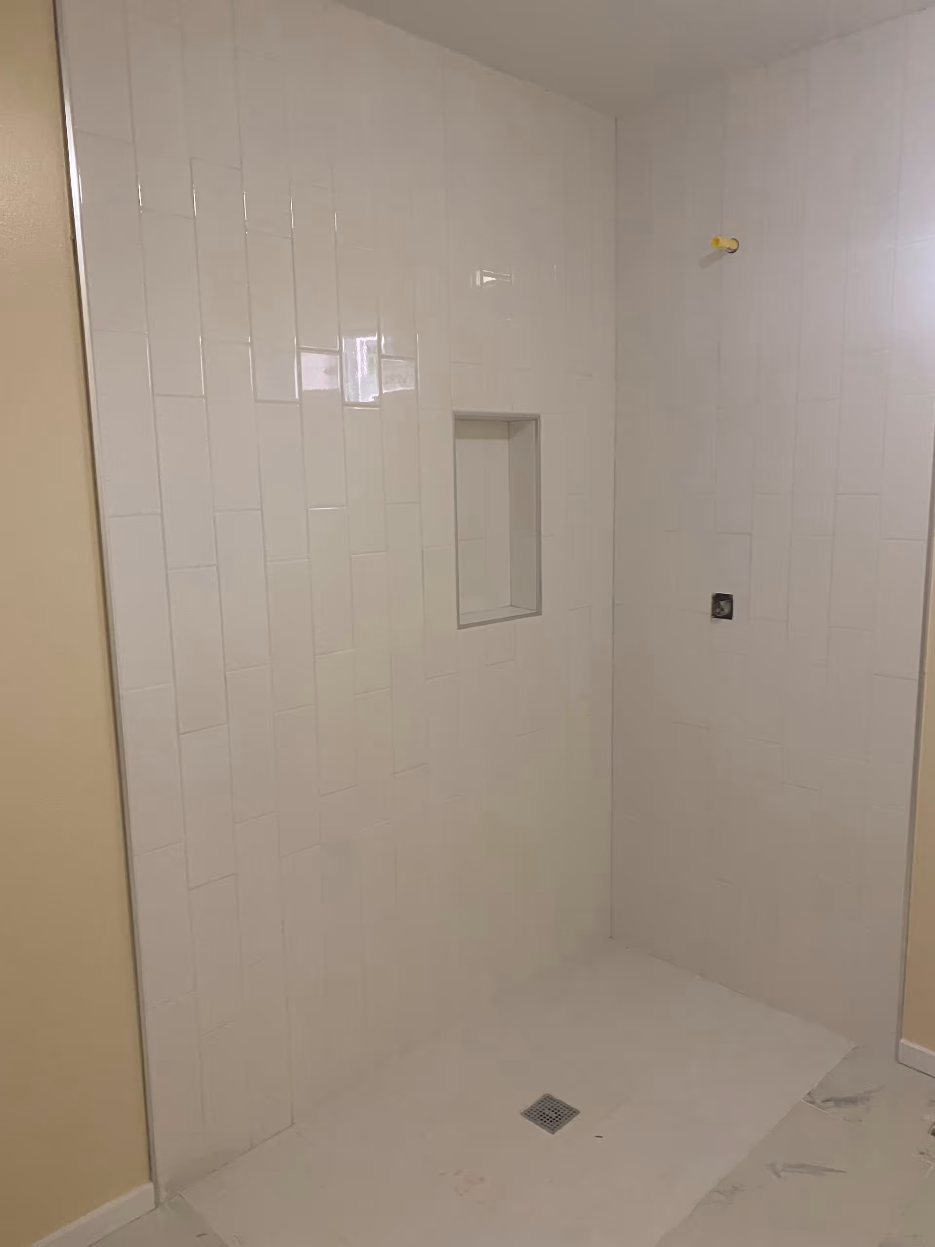 White tiled shower stall with a recessed niche, floor drain, and exposed shower plumbing stub.