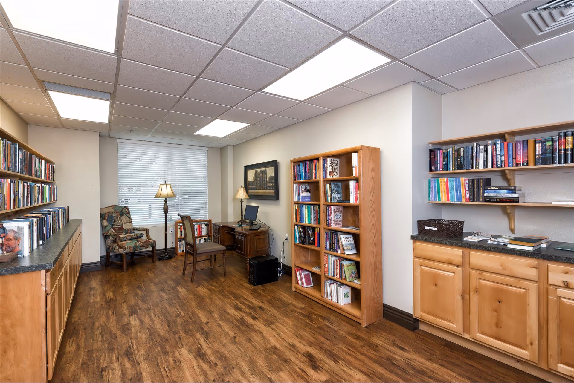 Small library/reading room with bookshelves, a desk, chairs, and lamps.