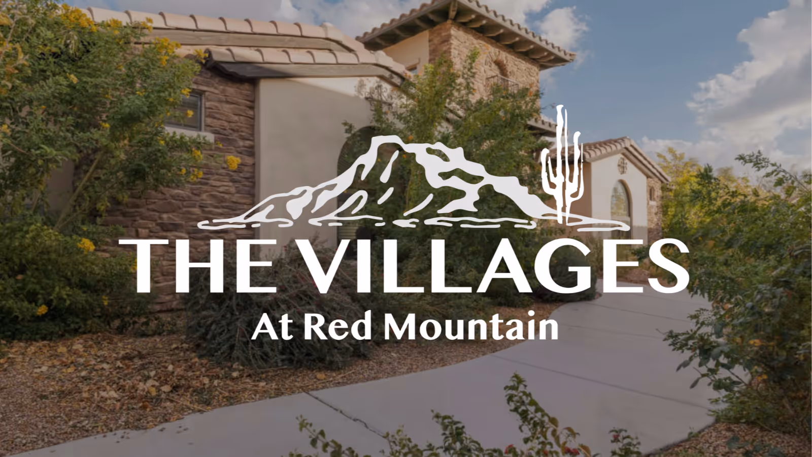 Exterior view of a residential building with stone and stucco walls, surrounded by desert landscaping including bushes and small trees, under a partly cloudy sky.