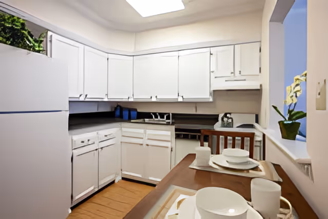 Small U-shaped kitchen with white cabinets, refrigerator, sink, and a breakfast bar set with dishes.
