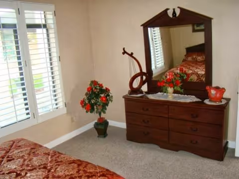 A cozy bedroom featuring a bed, dresser, mirror, and decorative plants.