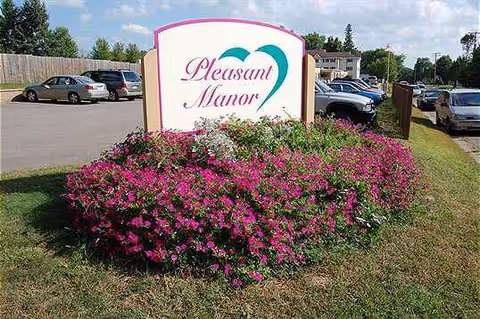 Pleasant Manor sign surrounded by pink flowering bushes in a parking lot.