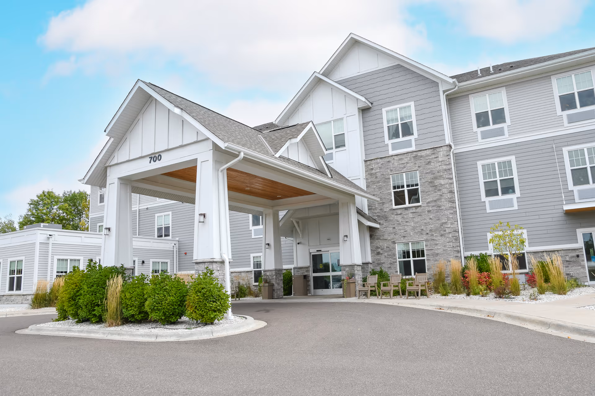 Front entrance of a multi-story senior living building with a covered porte-cochere, landscaping, and the address number 700.