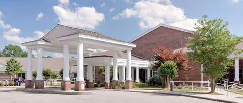 Exterior view of a senior living facility entrance with white columns and a brick building.