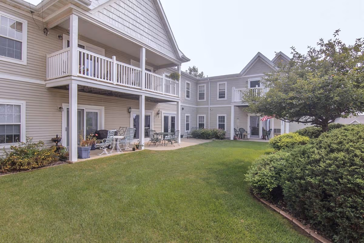 Two-story senior apartment building with balconies overlooking a grassy courtyard and patio seating.