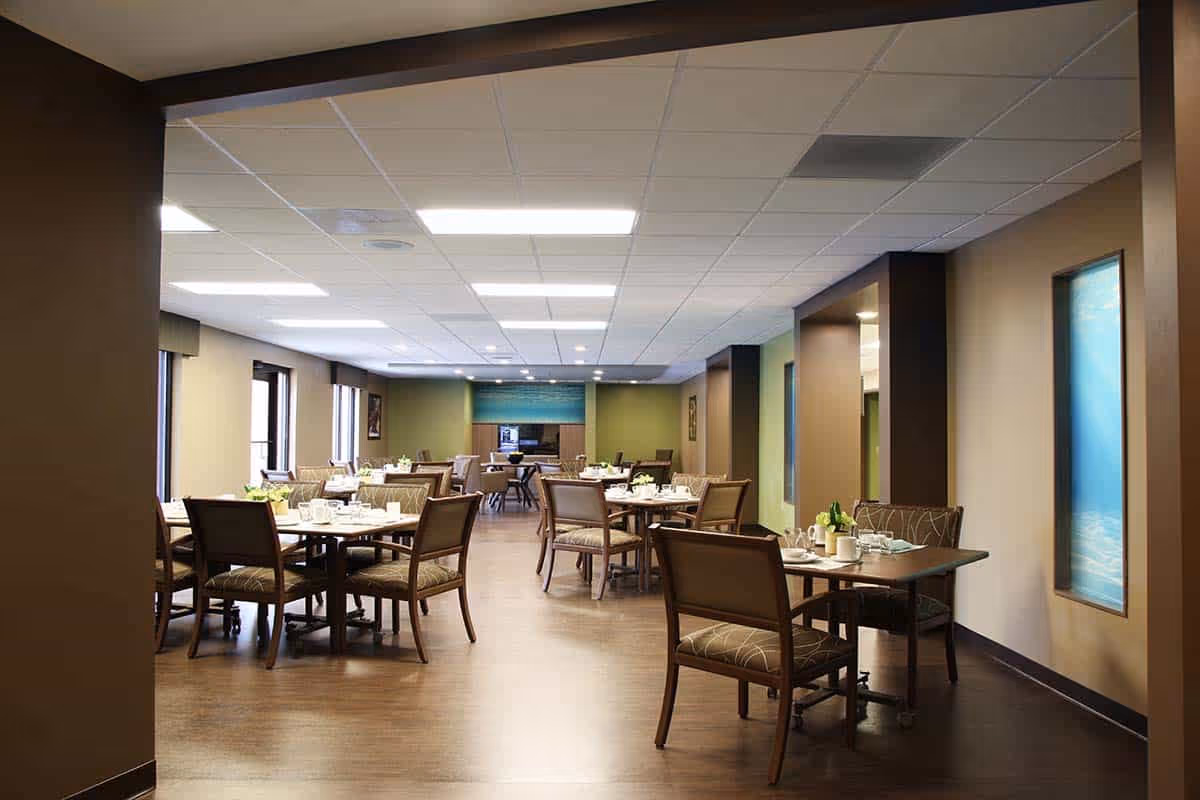 A large, modern dining room with multiple tables set for meals inside a senior living facility.