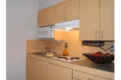 Small kitchen area with light wood cabinets, a microwave, a stovetop with two burners, a sink, and a decorative bowl on the counter.