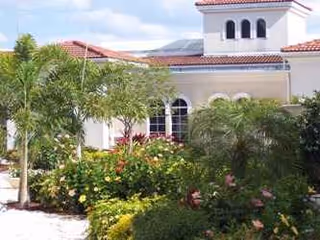 Front exterior view of a cream-colored senior living facility with palm trees and landscaping.