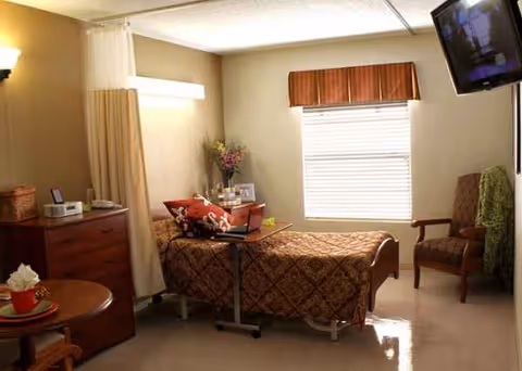 Nursing room with adjustable bed, privacy curtain, dresser, chair, and window blinds.