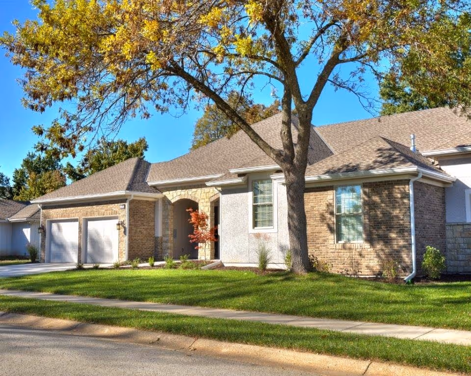 Single-story brick house with an attached two-car garage, front lawn, and a large tree in the yard.