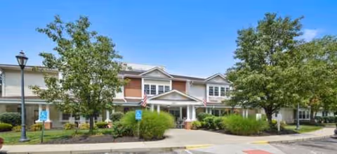 Front exterior of Outlook Manor senior living facility with entrance, shrubs, and trees.