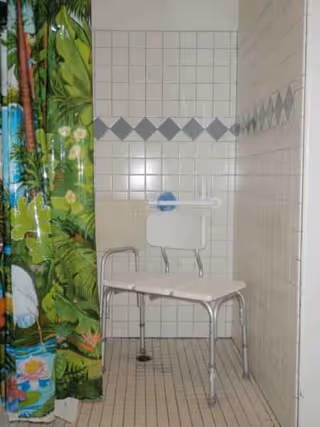 Tiled bathroom with a jungle-themed curtain and a metal-legged shower chair.