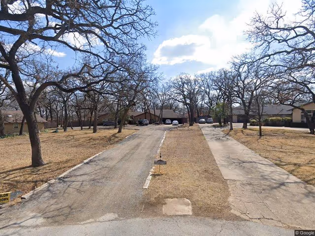 A view of the exterior driveway at Enhancing Life Care, lined with bare trees and a gravel path leading to parked cars and buildings in the background under a partly cloudy sky.
