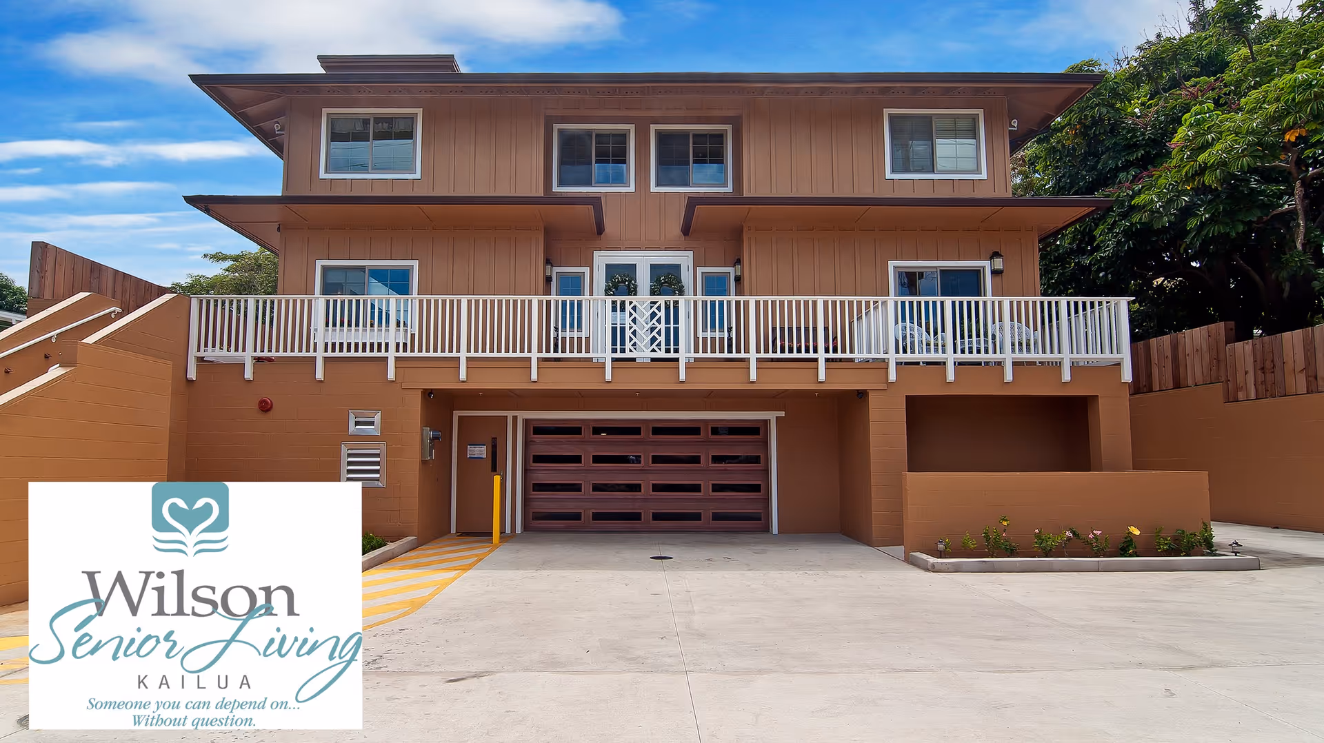 Exterior view of a two-story brown building with a white balcony railing and a garage door on the ground level under a clear blue sky.