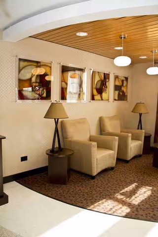 Two beige armchairs with side tables and lamps sit in a curved ceiling lounge area.
