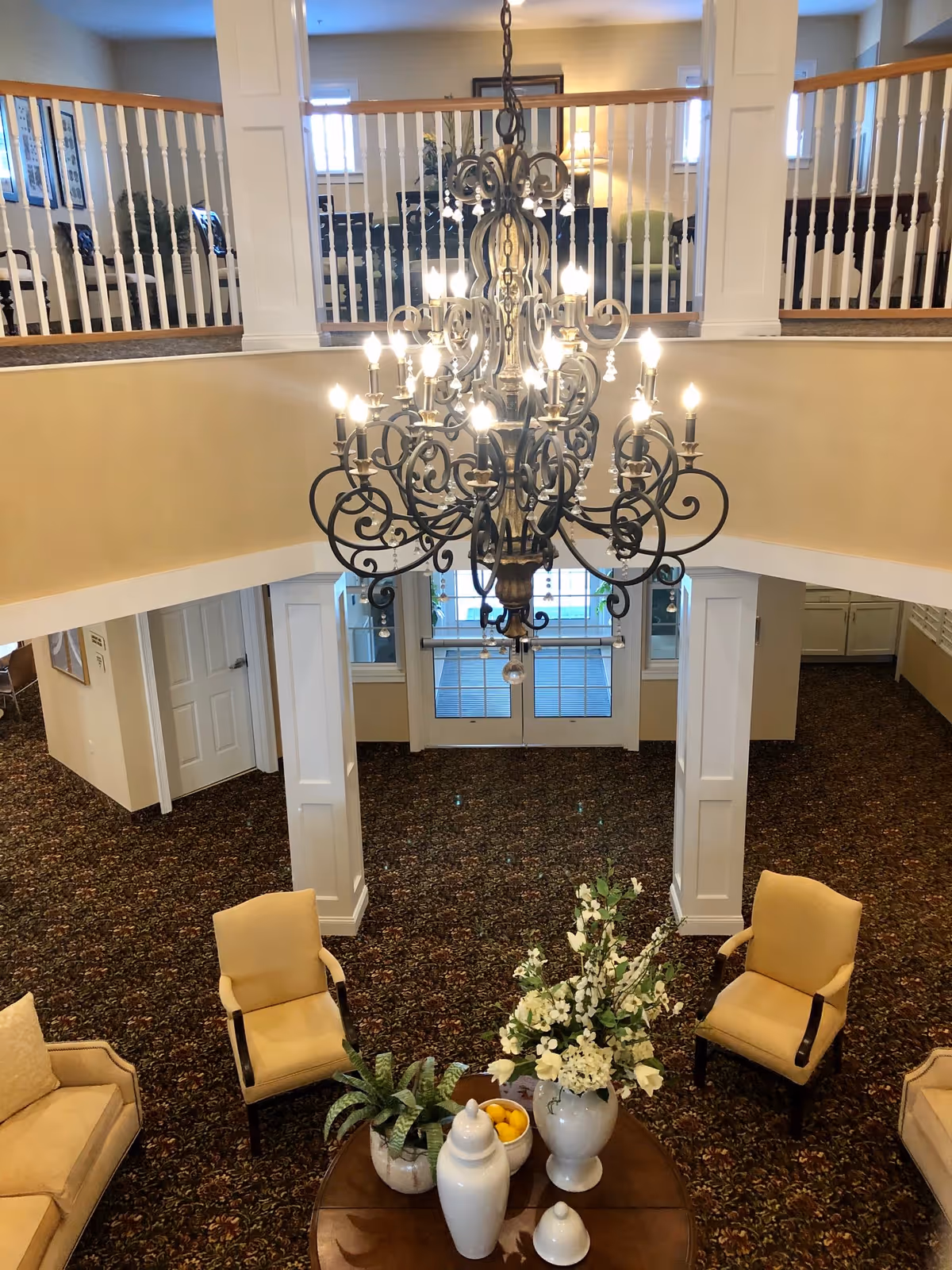View down into an elegant senior living lobby with a large ornate chandelier, seating, and a floral centerpiece on a table.