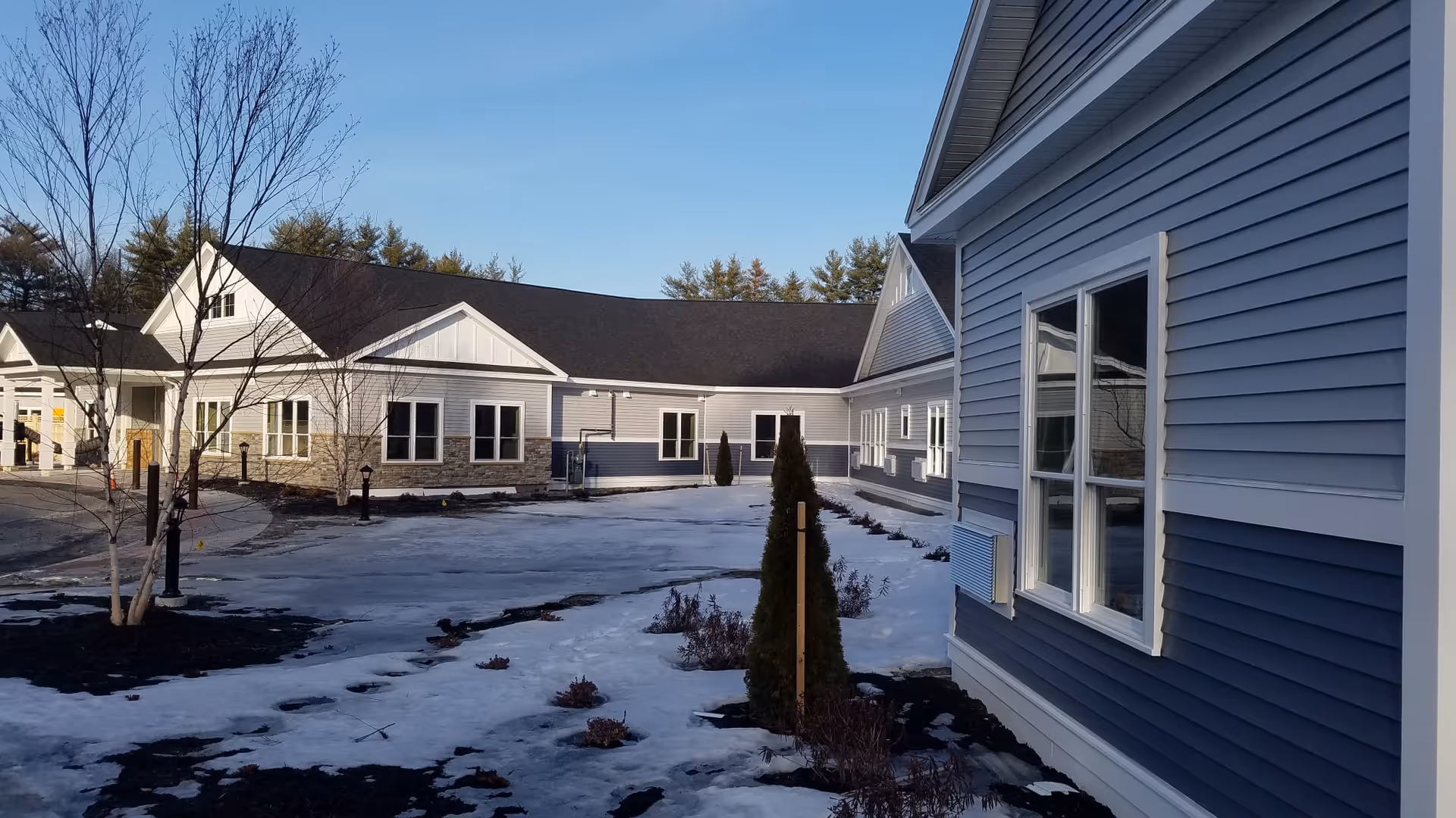Exterior view of the Summer Commons senior living buildings and courtyard with snow on the ground and blue-gray siding.