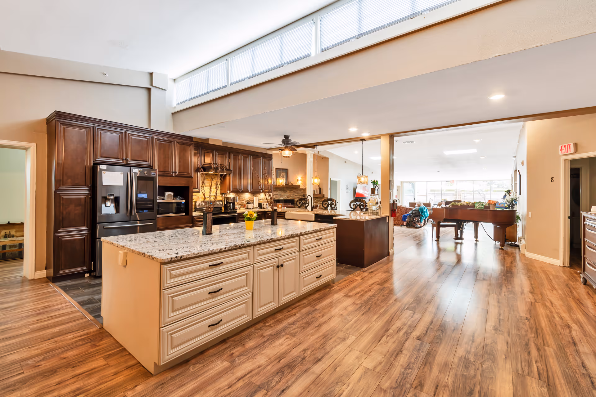 Open communal kitchen with a large island, dark wood cabinets, stainless appliances, and an adjoining lounge area with a piano.