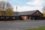 Single-story brick health and rehab building with a covered entrance, American flagpole, and a paved parking lot.