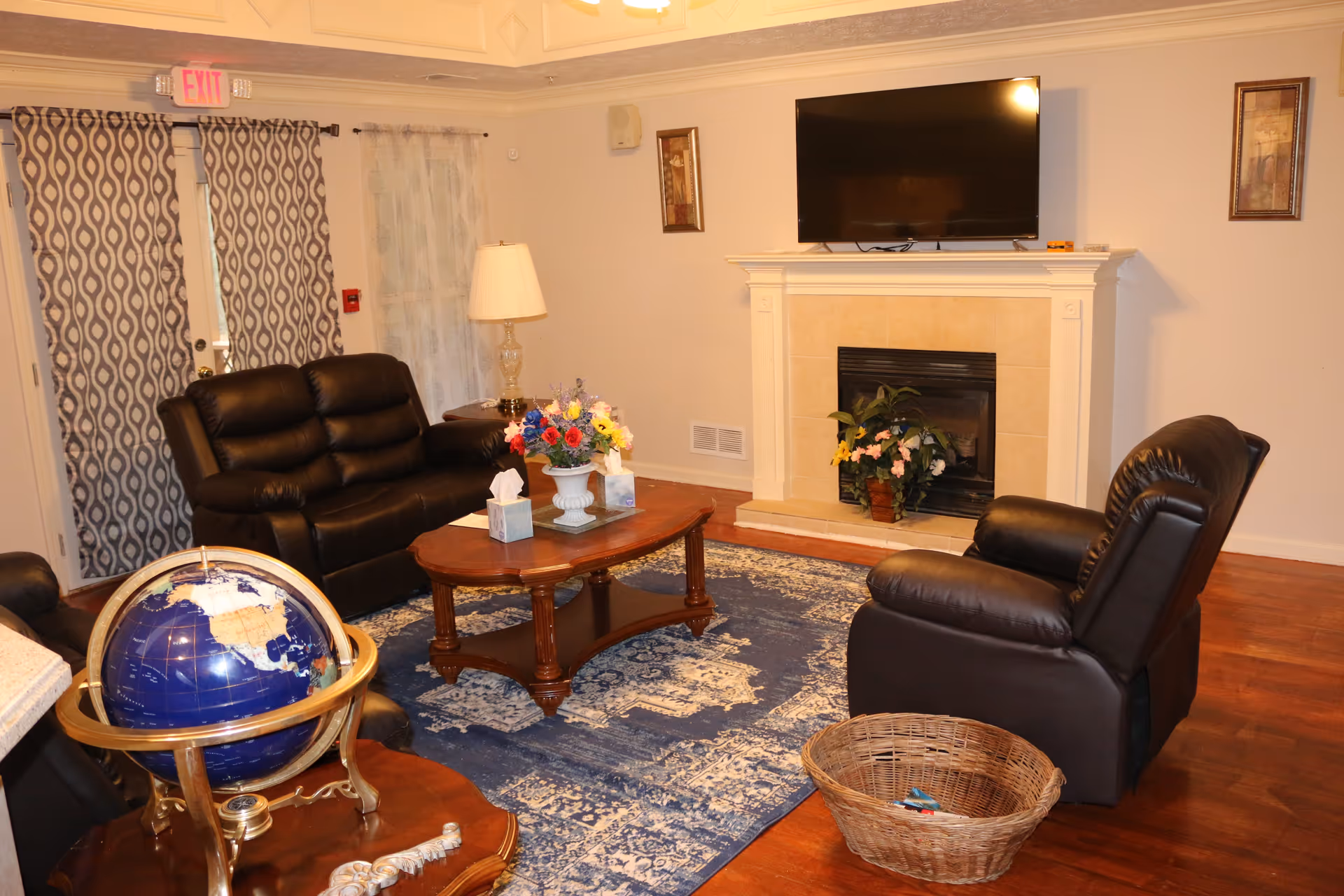Cozy living room with leather recliners around a wooden coffee table, a fireplace with a wall-mounted TV, and a globe on a side table.