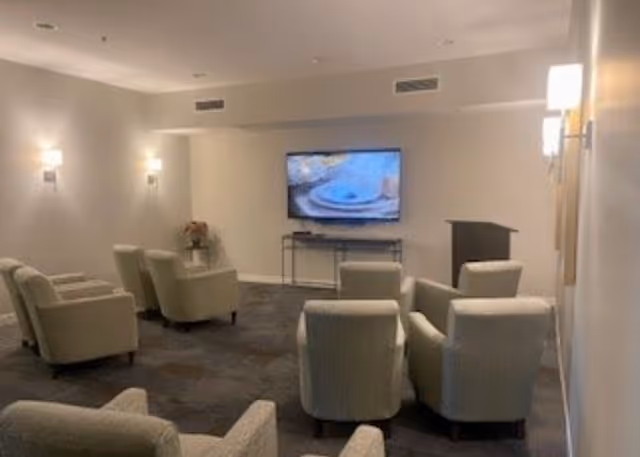 Small communal media room with several upholstered armchairs facing a wall-mounted television and a podium.