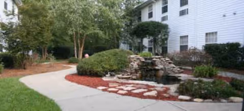 Well-maintained exterior of a senior living building with a stone fountain and landscaped walkway.