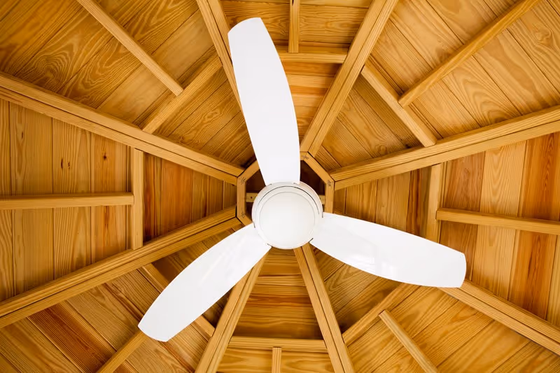 White three-blade ceiling fan mounted on a wooden gazebo ceiling with radial beams.