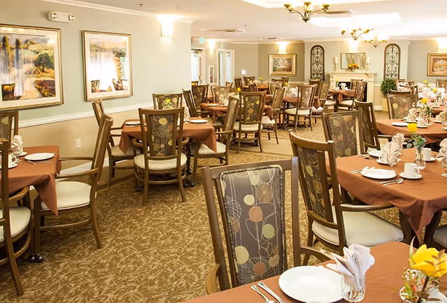 Large communal dining room with round tables covered in brown tablecloths, place settings, and patterned chairs.
