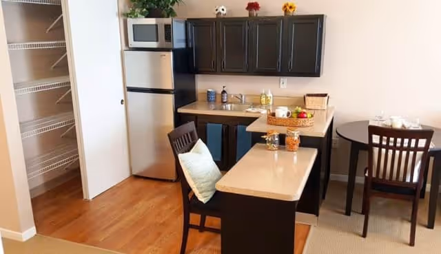 A modern kitchen interior featuring a countertop, dining table, and appliances including a refrigerator and microwave.