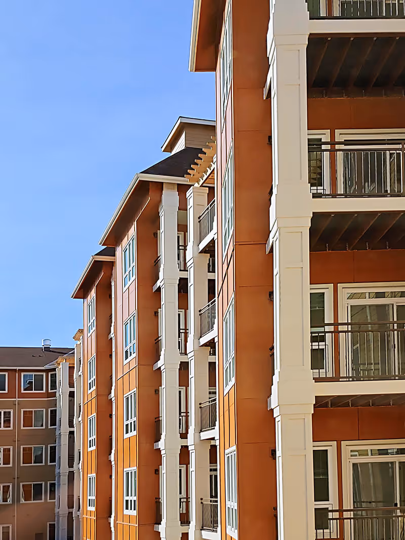Exterior view of a multi-story residential building with orange and white facade, featuring balconies and large windows under a clear blue sky.