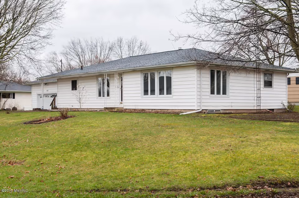 Single-story white house with a green lawn and leafless trees under an overcast sky.