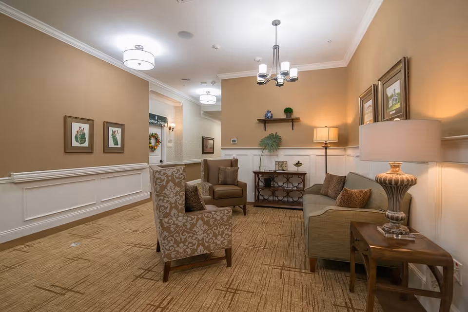 A cozy furnished sitting area with armchairs, a sofa, side tables, lamps, and wall art in a warm-toned interior.