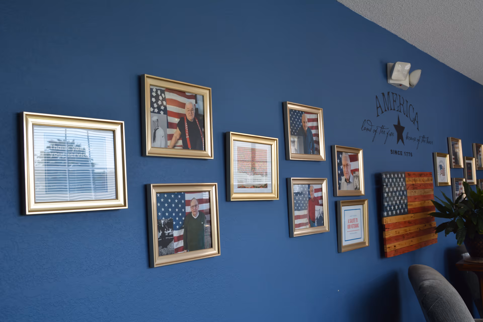 Blue interior wall decorated with gold-framed portraits and American flag–themed artwork in a senior living facility common area.