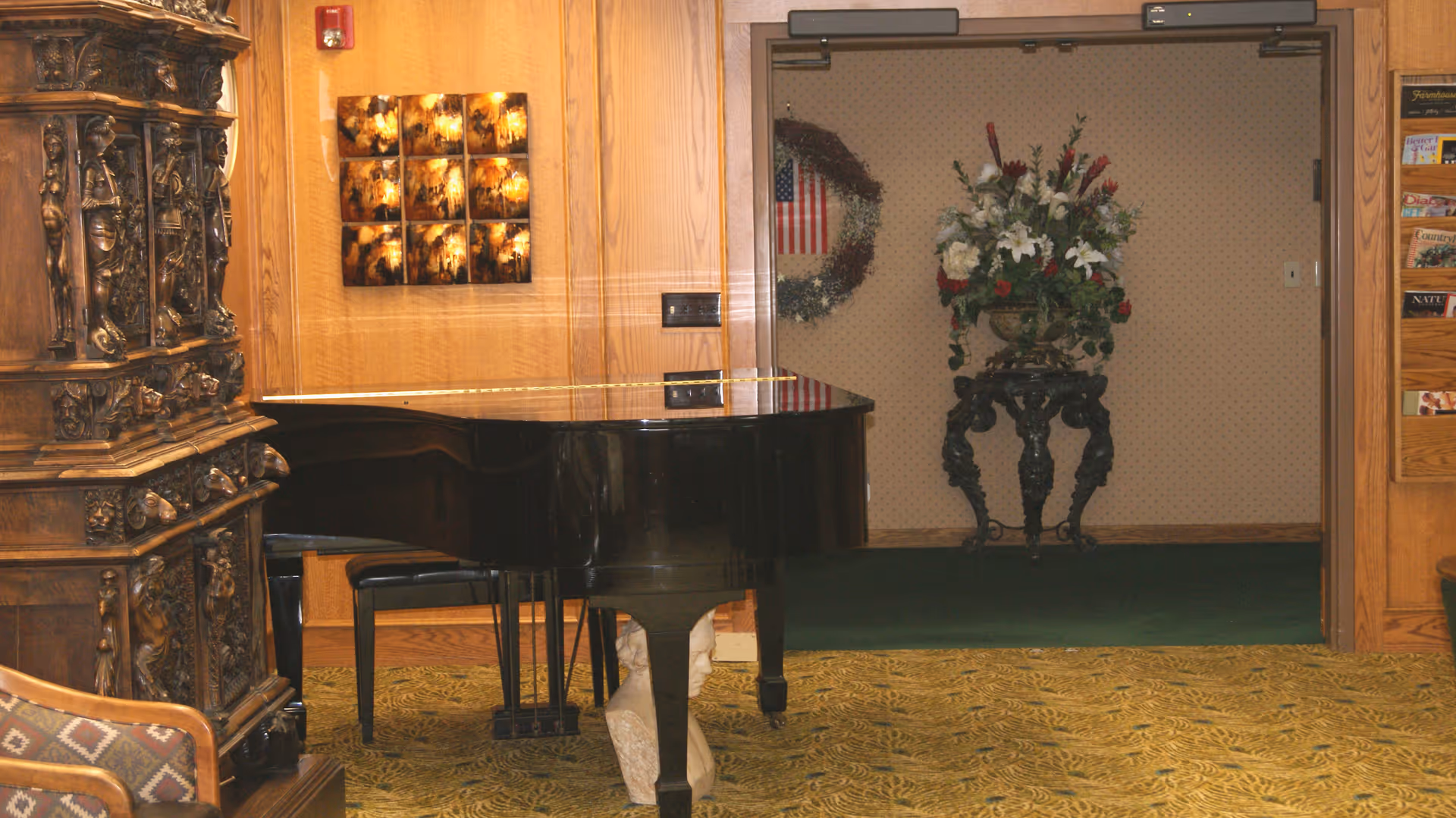 Interior common area with a black grand piano, ornate wooden furniture, and a floral arrangement in an adjacent alcove.