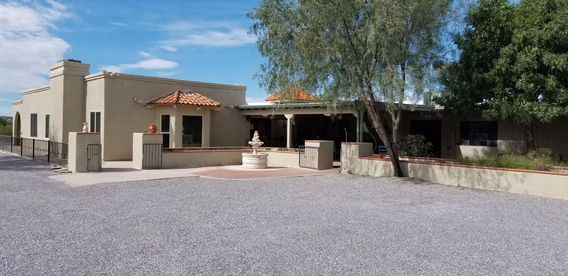Single-story stucco assisted living building with a tiled awning and central fountain in a gravel courtyard.
