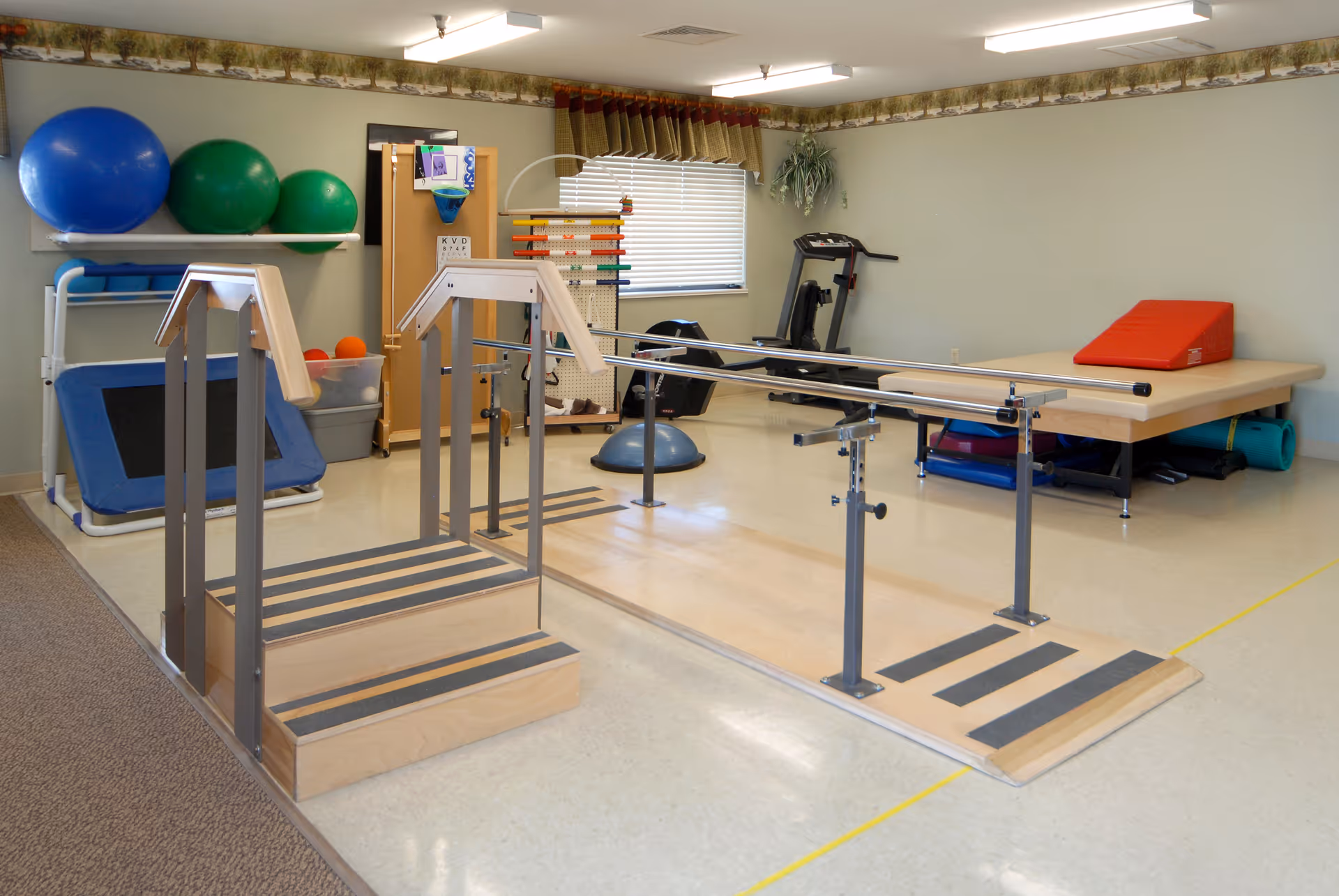 A physical therapy room with parallel bars, exercise equipment, a treatment table and large exercise balls.