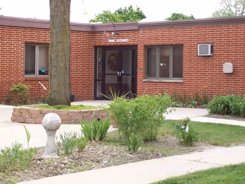Brick facility entrance with glass doors, landscaping, and a Main Entrance sign.
