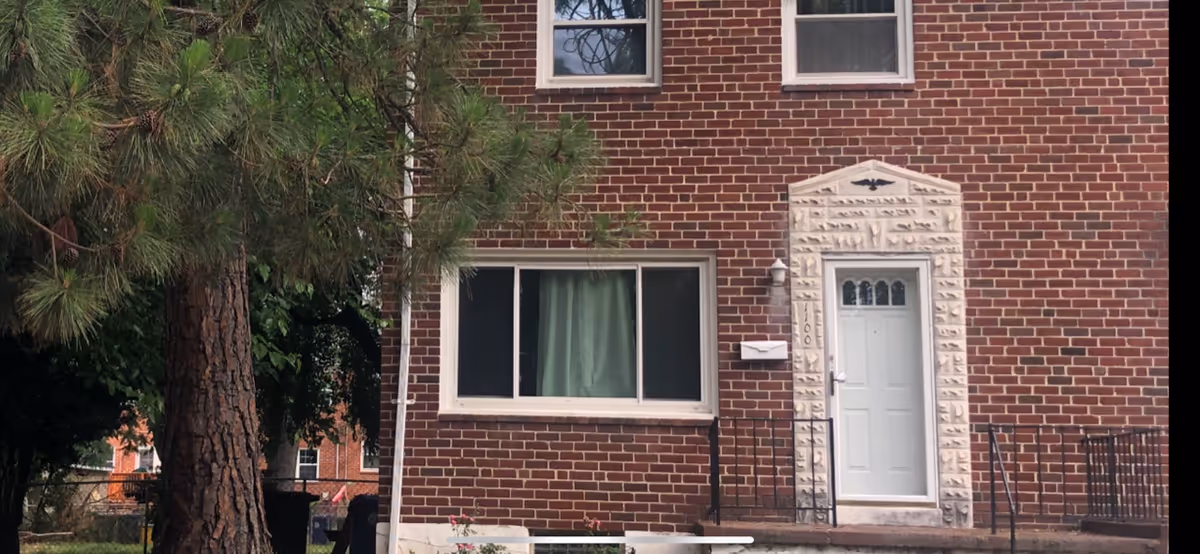 Brick senior living building exterior with a white door, large window, and pine tree.