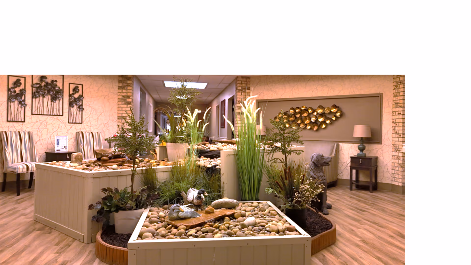 An indoor common area with raised planter boxes filled with stones and plants, seating, and wall decor.