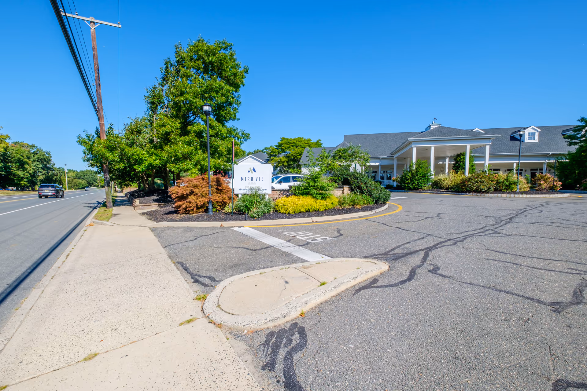 Driveway entrance and landscaped sign for Mira Vie assisted living with the building's front under a clear blue sky.