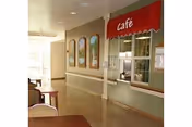 Interior corridor with a small café serving window under a red 'Café' awning, seating area, handrail, and decorative wall panels.