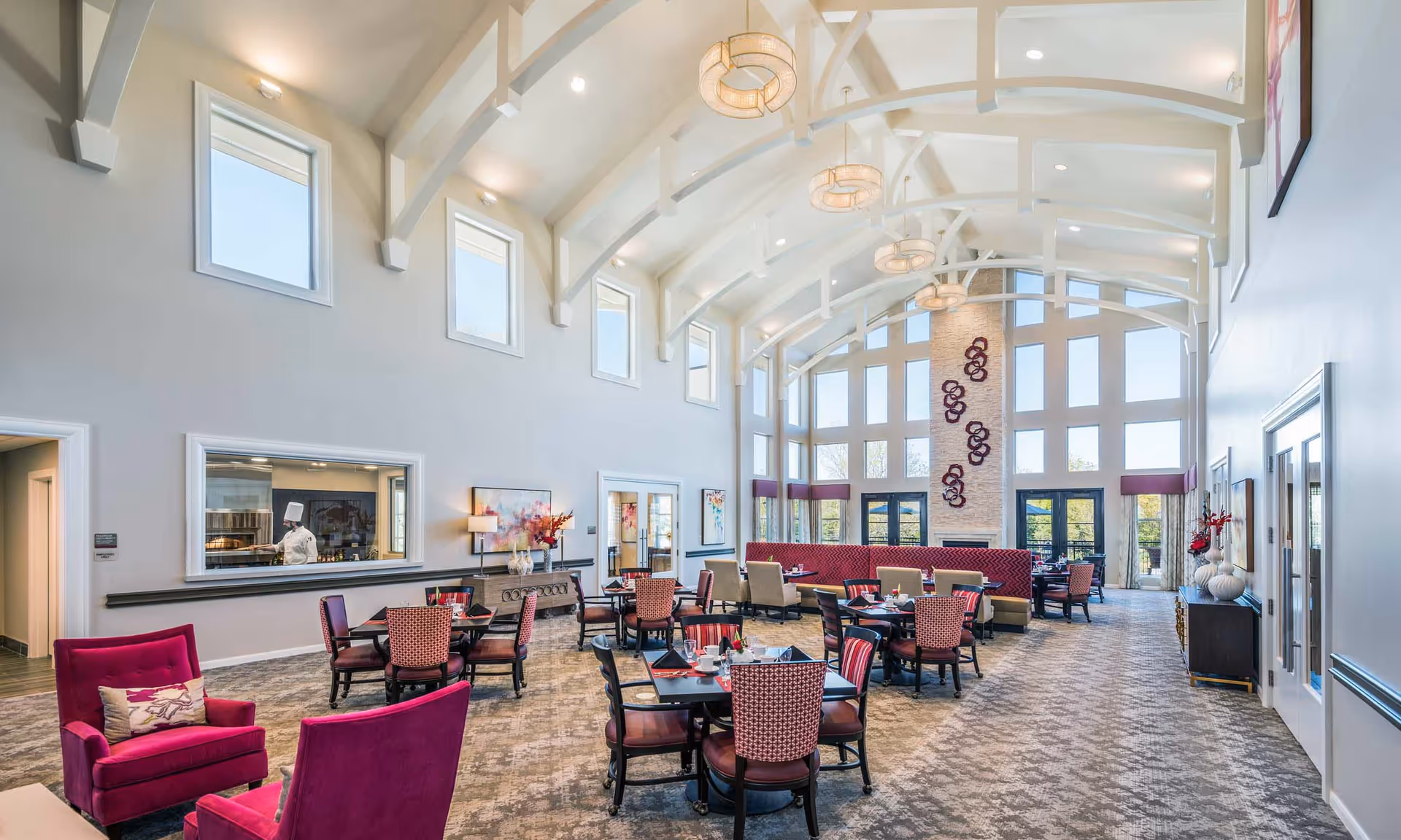 Bright, open dining room with vaulted beams, large windows, round tables and upholstered seating.