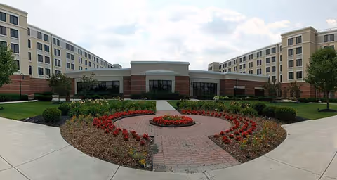 Front exterior of a multi-story senior living building with a circular brick driveway and landscaped courtyard.