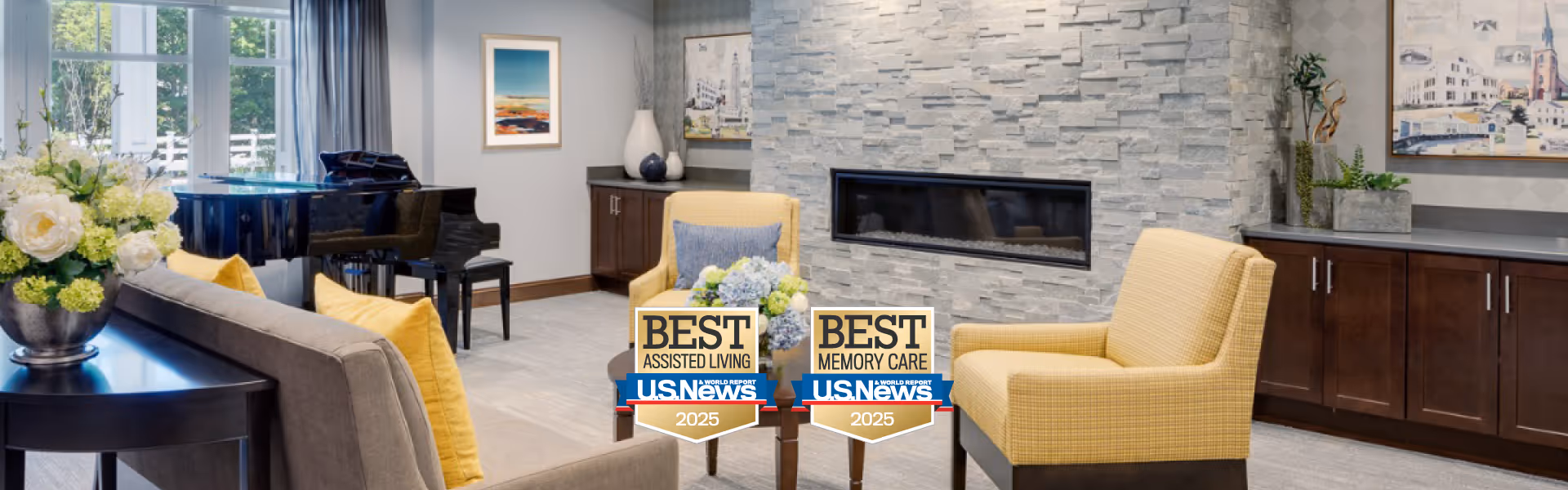 A cozy living room area in an assisted living facility featuring a gray sofa with yellow pillows, two yellow armchairs, a modern stone fireplace, a black grand piano near a window with blue curtains, and a dark wooden sideboard with decorative items and artwork on the walls.