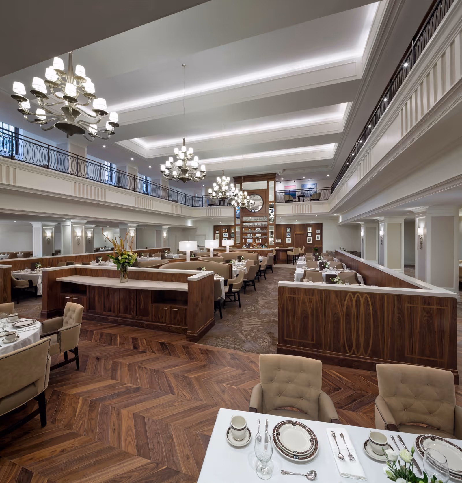 Large elegant two-story dining room with chandeliers, wood-paneled booths, and neatly set tables.