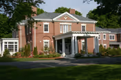 Brick assisted living building with a covered entrance, manicured landscaping, and a driveway in front.