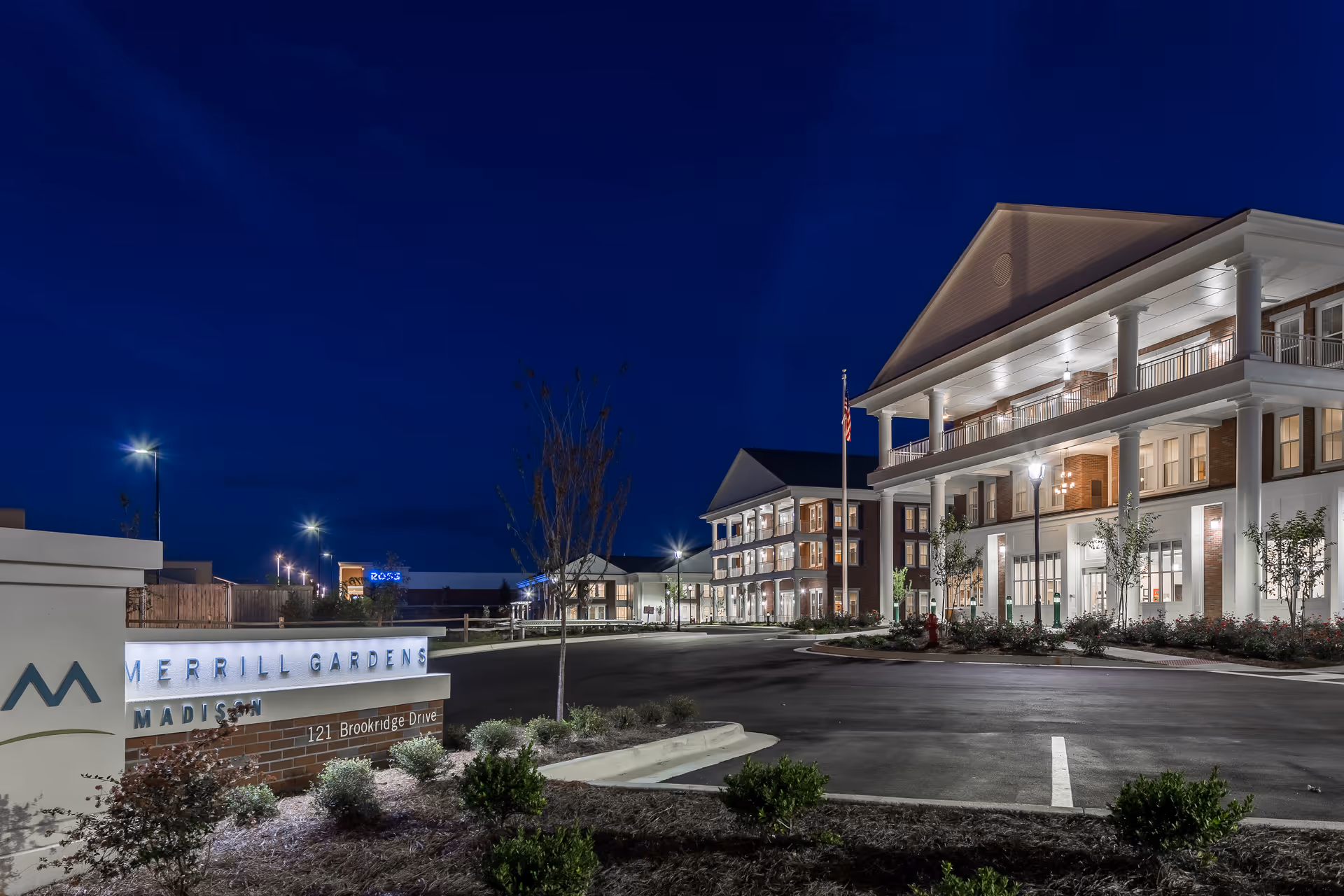 Nighttime exterior view of the illuminated Merrill Gardens at Madison building and entrance with visible signage.